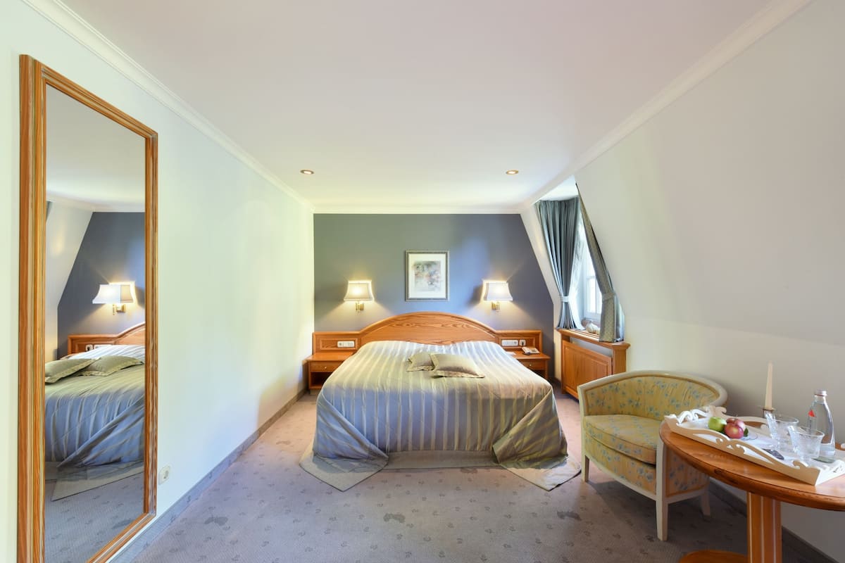 A hotel room with a bed, bedside tables, a chair, a table with a tray, and a mirror.