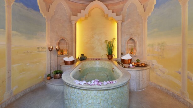 Une salle de bain luxueuse avec une grande baignoire sur pieds, des plantes décoratives et une fresque représentant un paysage désertique.