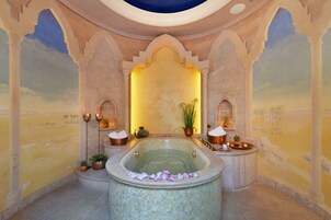 A luxurious bathroom with a large freestanding bathtub, decorative plants, and a mural of a desert landscape.