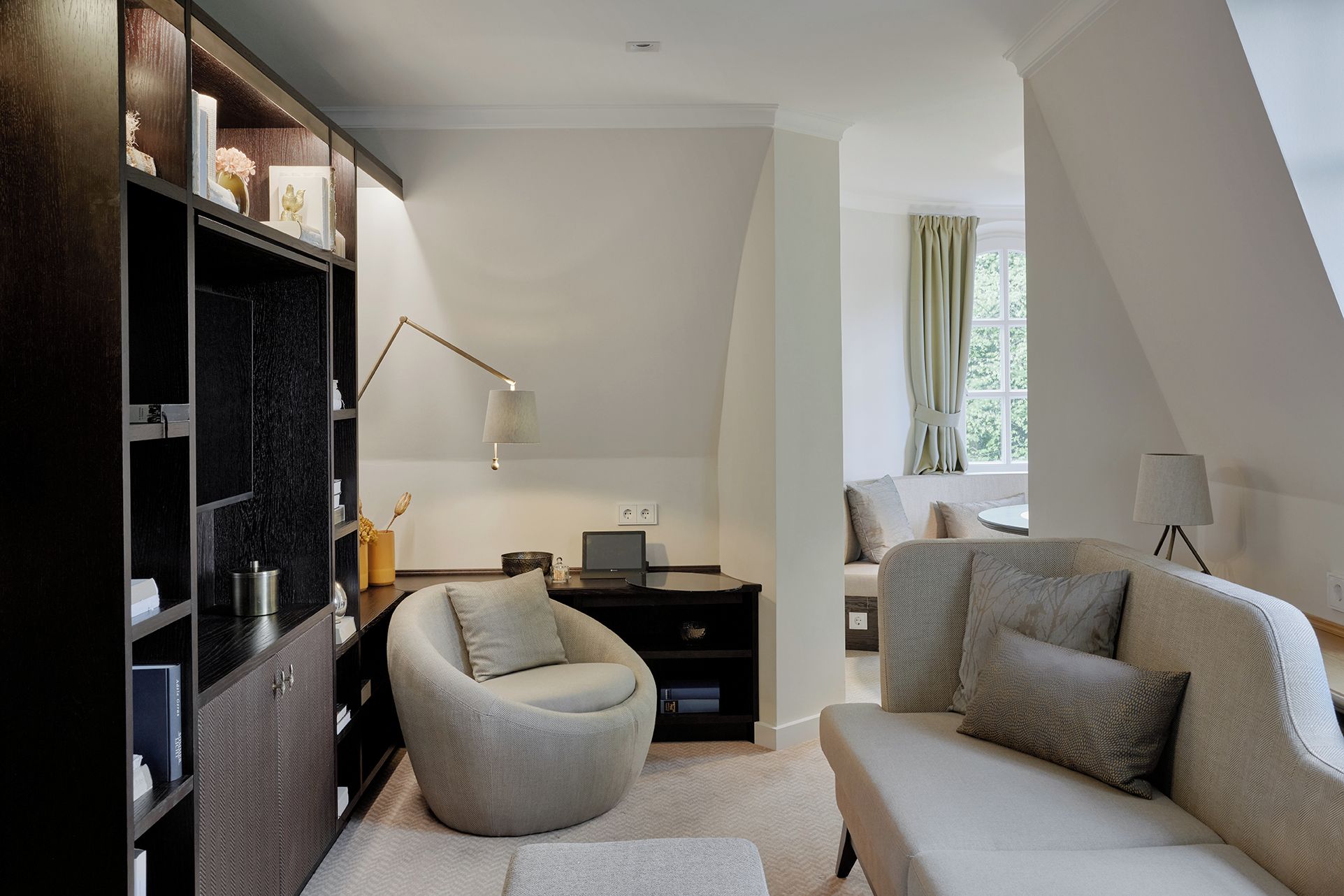 A modern living room with a round chair, a sofa, a desk with a lamp, and a bookshelf.