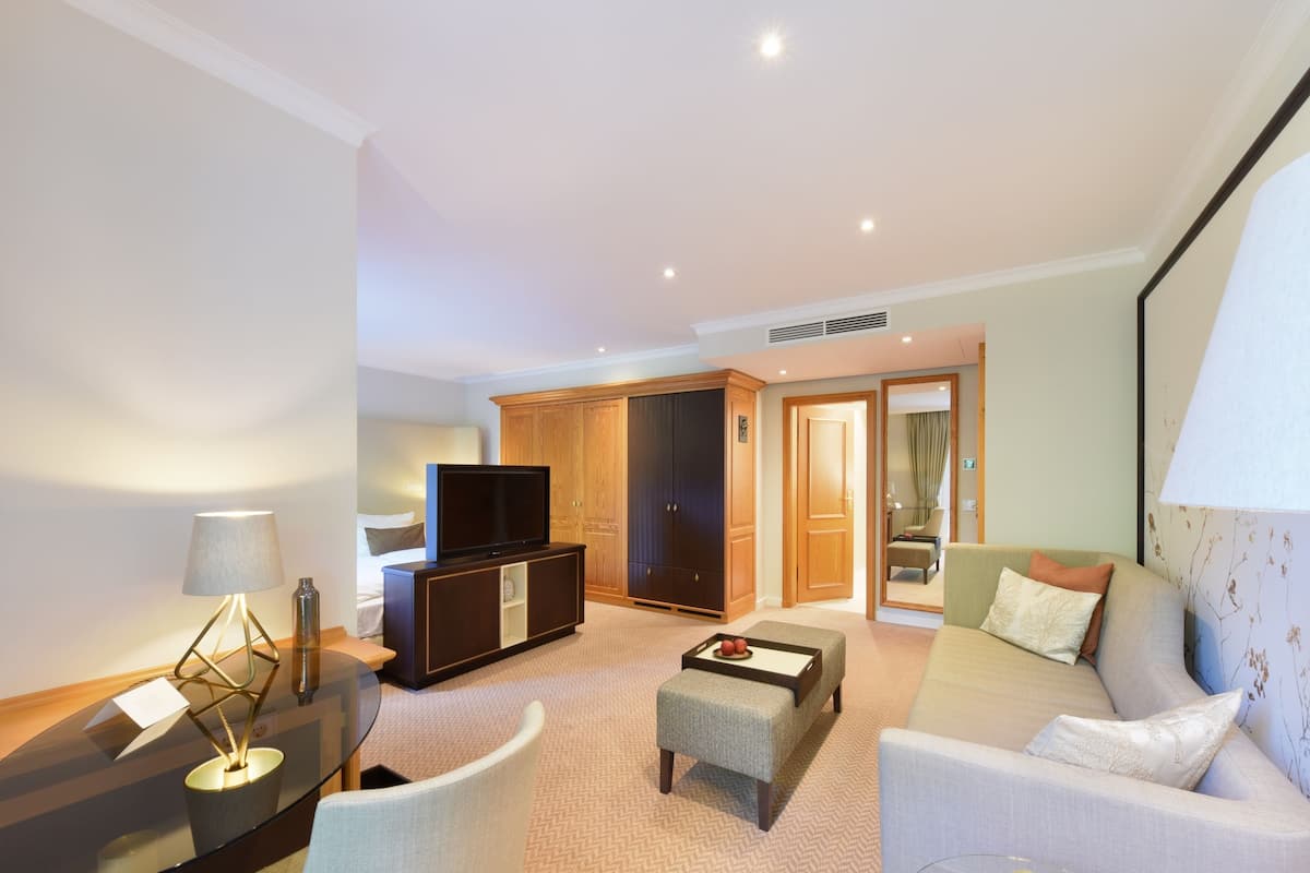 A modern hotel room with a sofa, a small table, a TV, and a cabinet.
