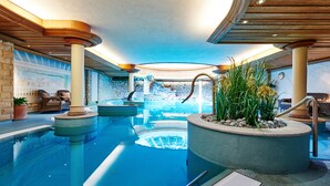 Une grande piscine intérieure avec vue sur une cascade, entourée de chaises longues et de plantes en pot.