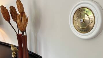 Un dispositivo fijado a la pared con la inscripción 'Ring for Champagne' y una figurita de pájaro sobre una superficie oscura.