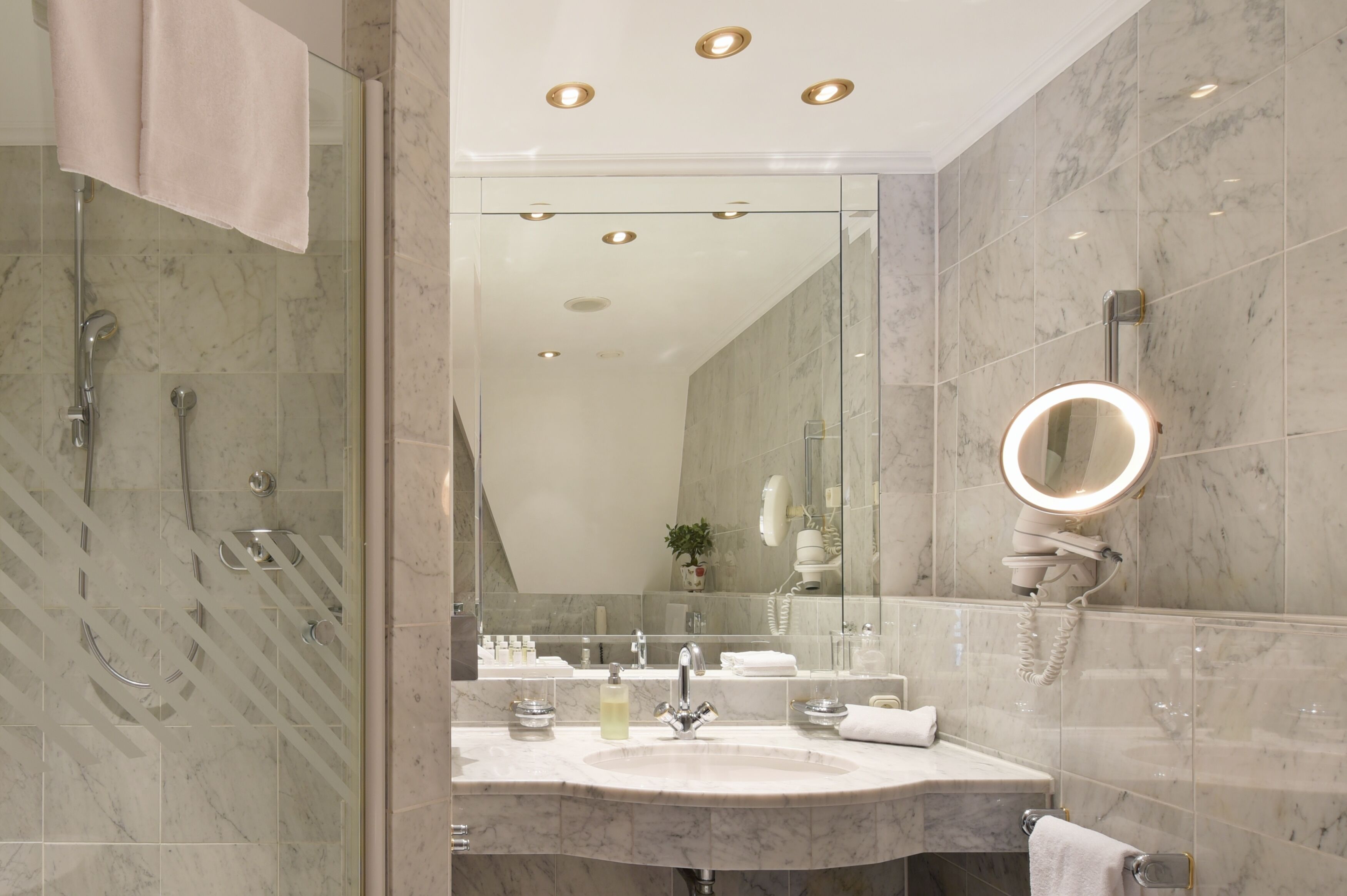 A modern bathroom with a glass-enclosed shower, a vanity with a mirror, and a marble-tiled wall.