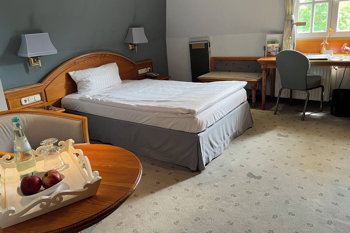 A hotel room with a bed, bedside tables, a desk, and a chair. There is a tray with apples and a bottle on the bed.