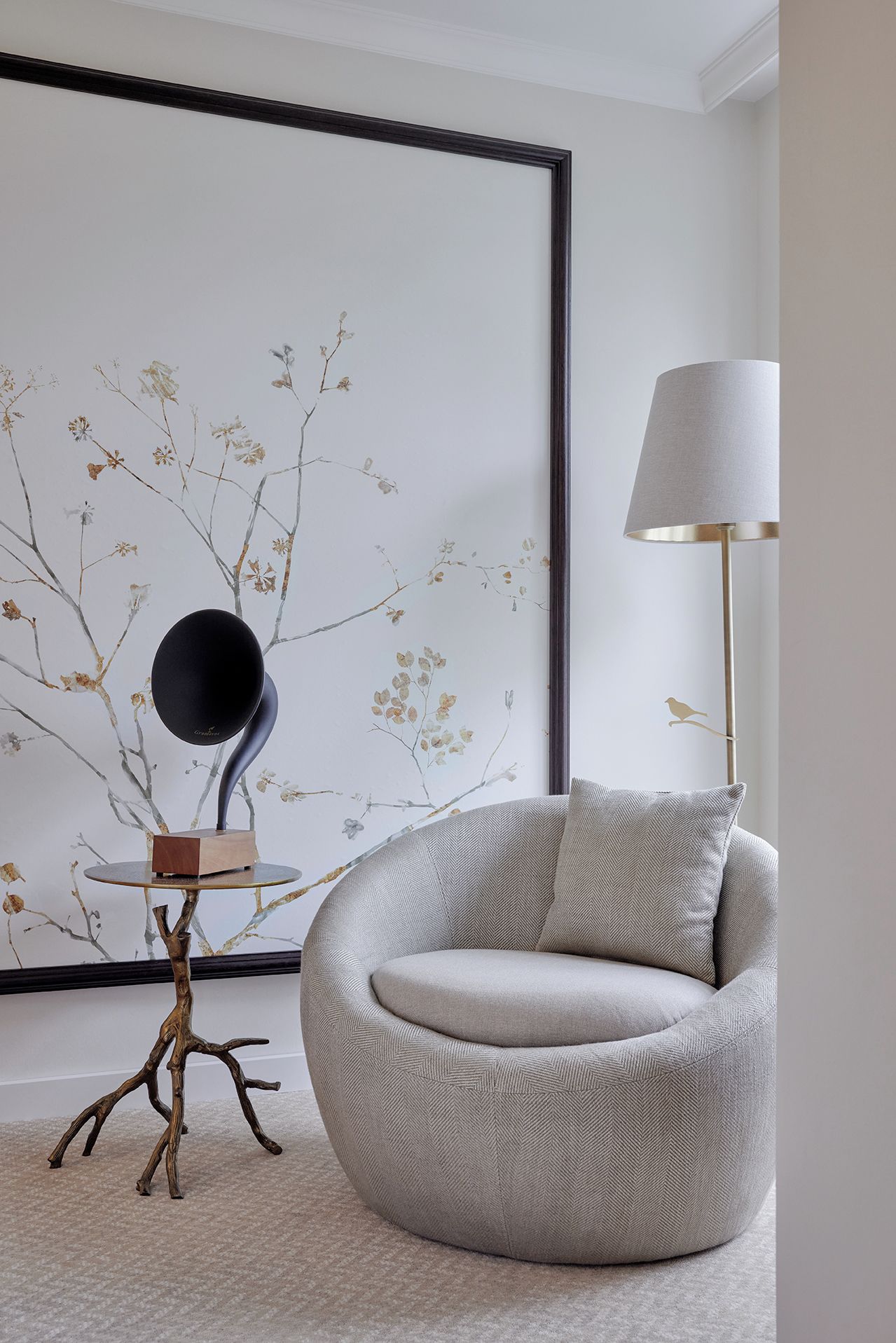 Una sala de estar moderna con un sillón redondo, una mesita con una lámpara original y una gran obra de arte en la pared.