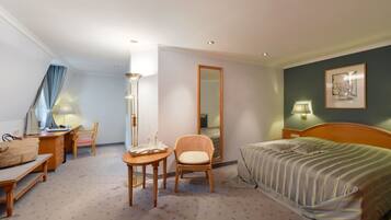 Una habitación de hotel con cama, escritorio, silla, una mesita, espejo y lámpara.