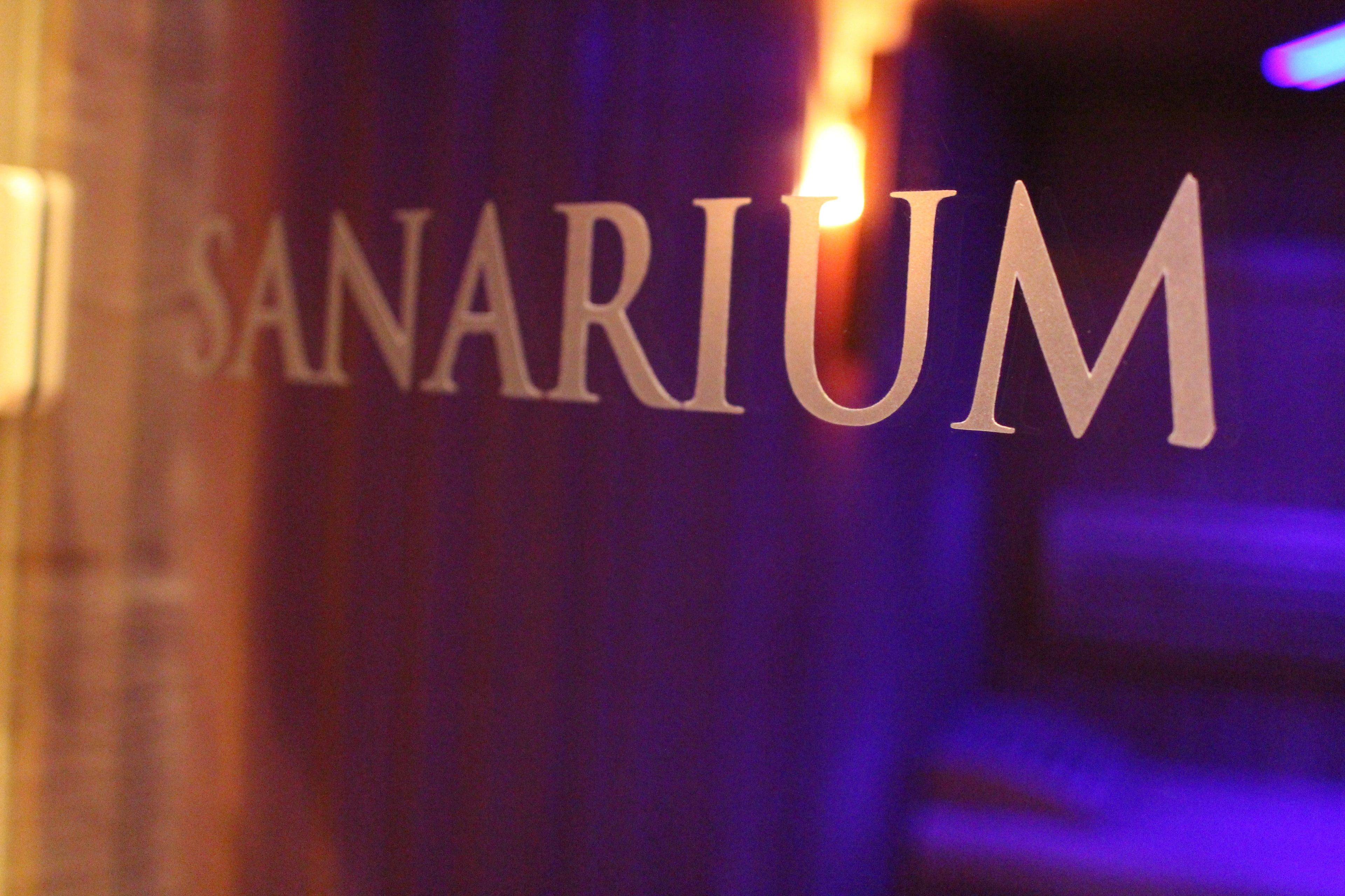 Ein Detailbild des Wortes "SANARIUM" in einer fetten, Serif-Schrift auf dunklem Hintergrund.
