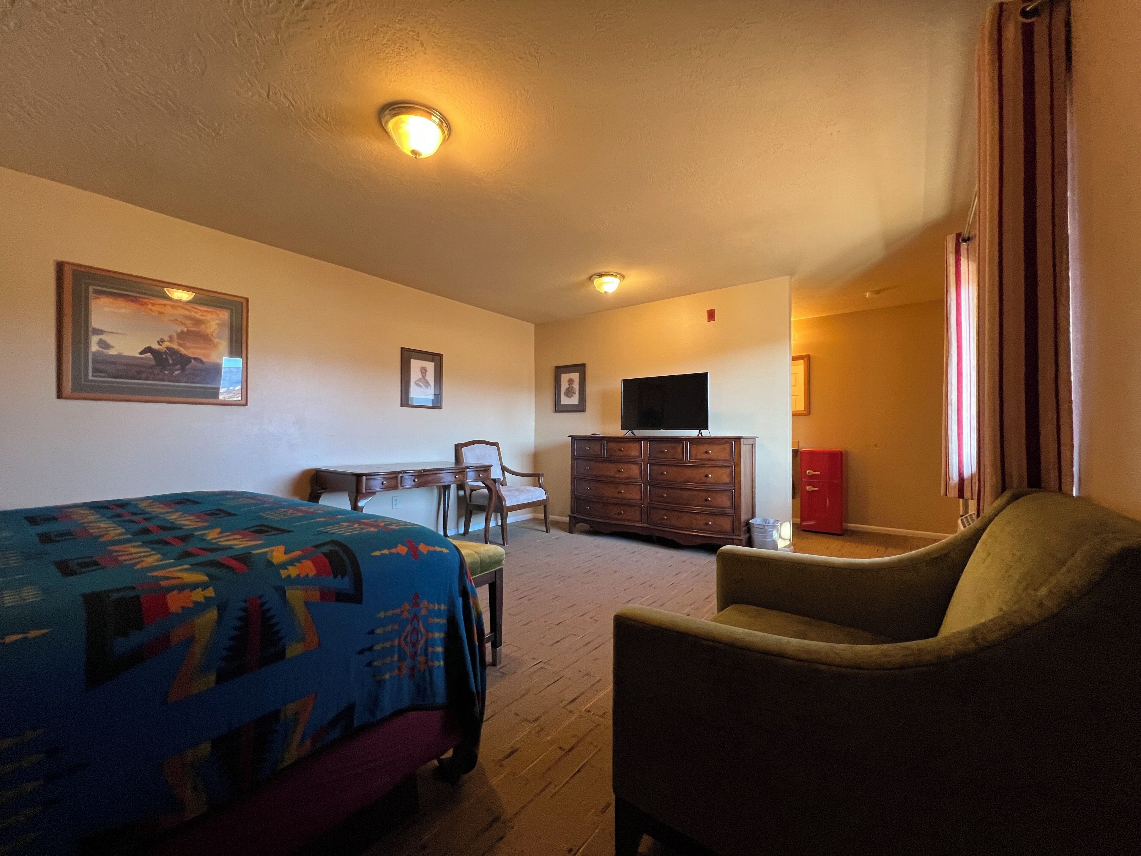 A room with a bed, a chair, a dresser, a television, and a painting on the wall.