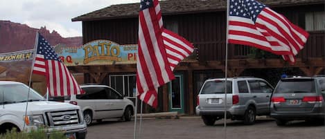A parking lot with several cars and American flags in front of a building with a sign that reads "Patio Rock Pit BBQ".