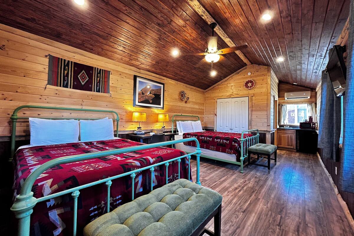 A cozy log cabin room with two beds, a bench, a ceiling fan, and a painting on the wall.