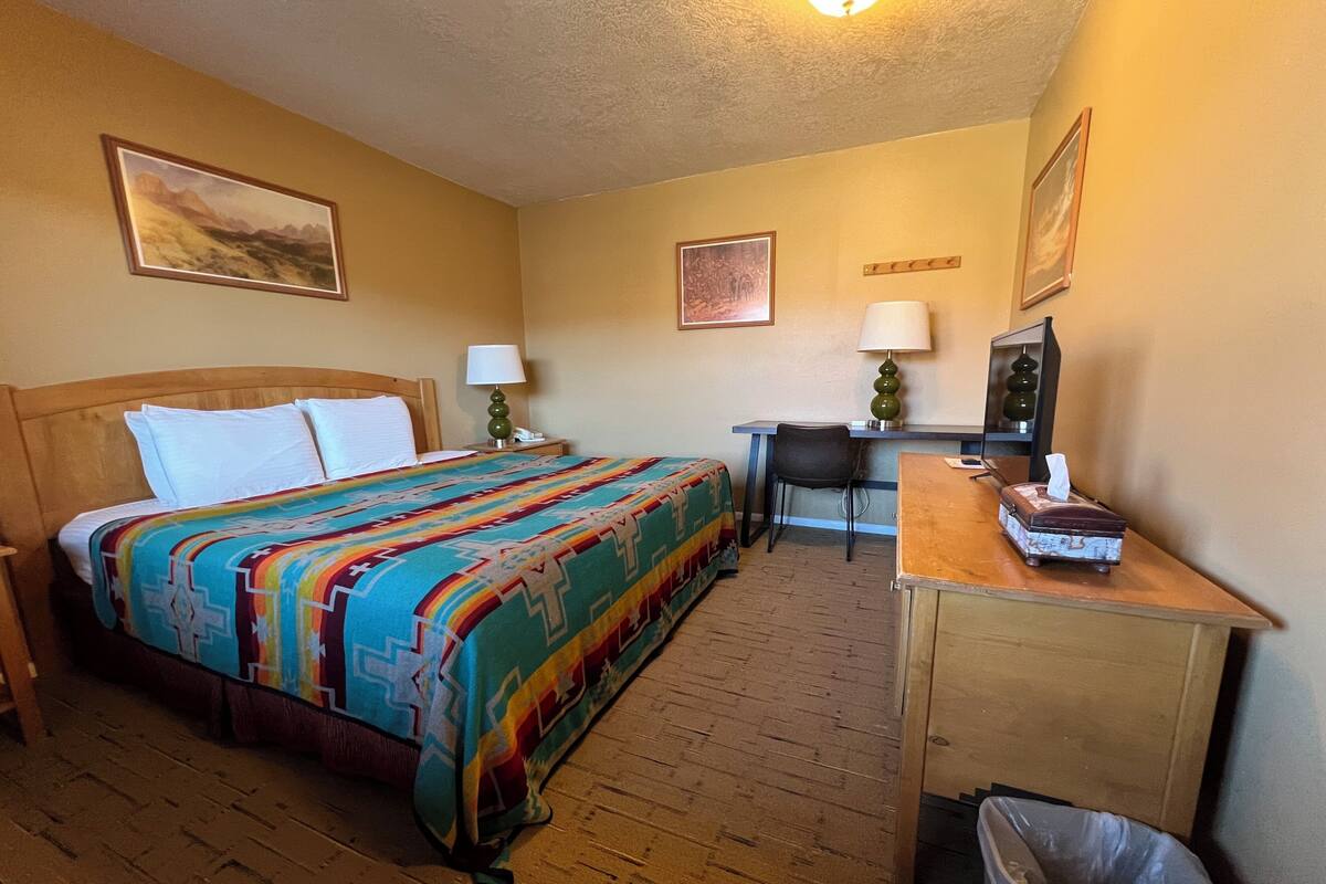 A hotel room with a wooden bed, a desk, a chair, and a trash bin.