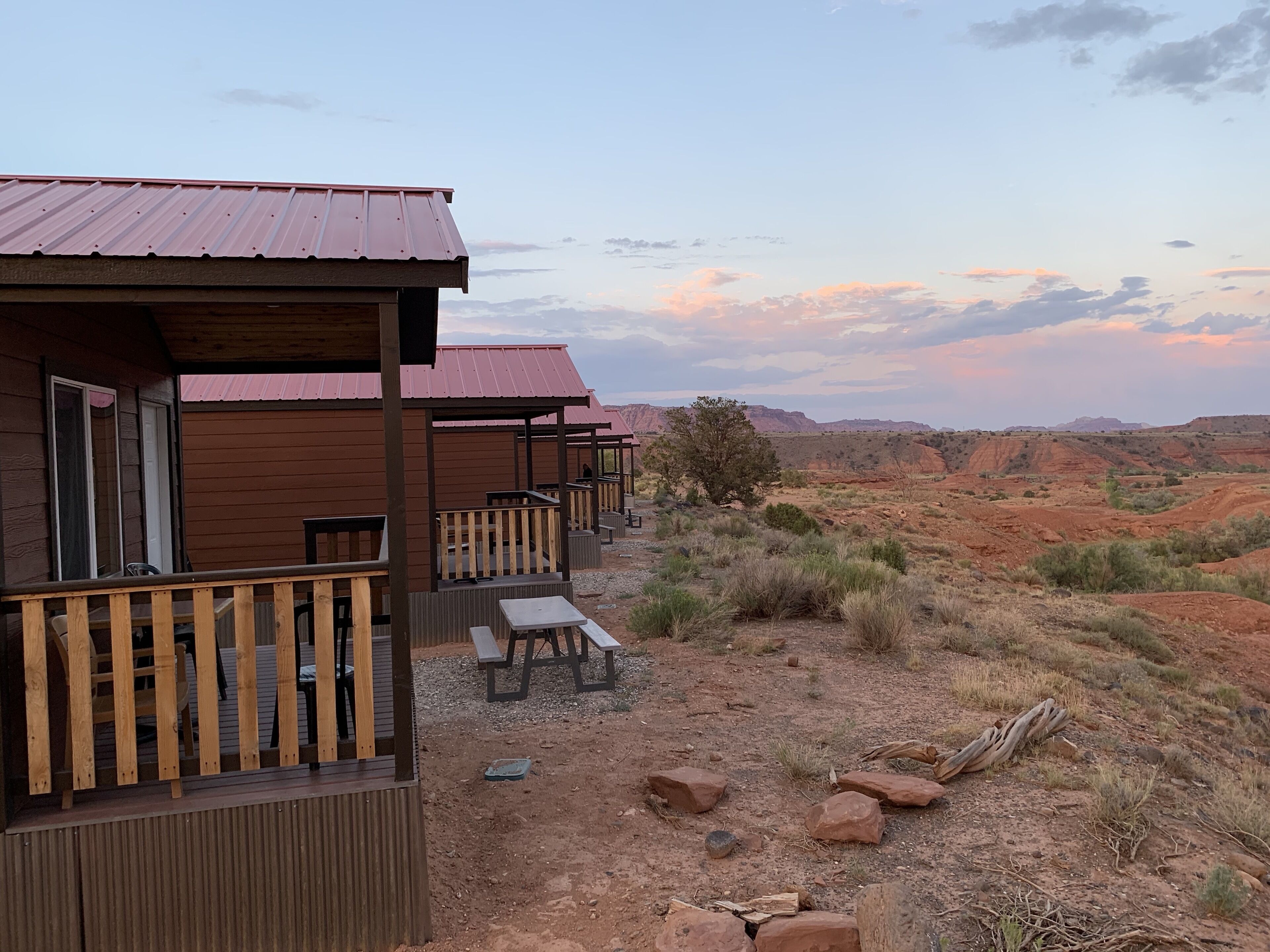 A row of wooden cabins with metal roofs, each featuring a wooden deck and a picnic table.