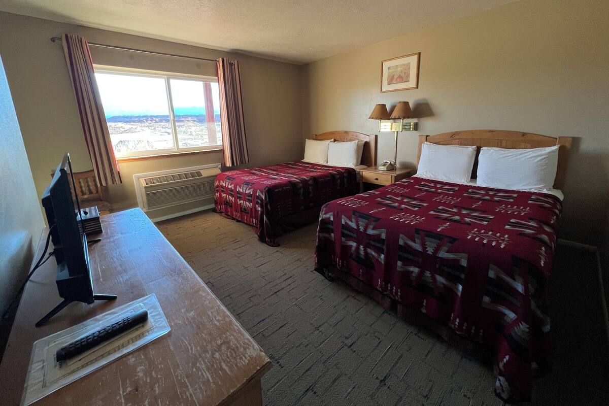 A hotel room with two beds, a desk, a computer, and a window with curtains.
