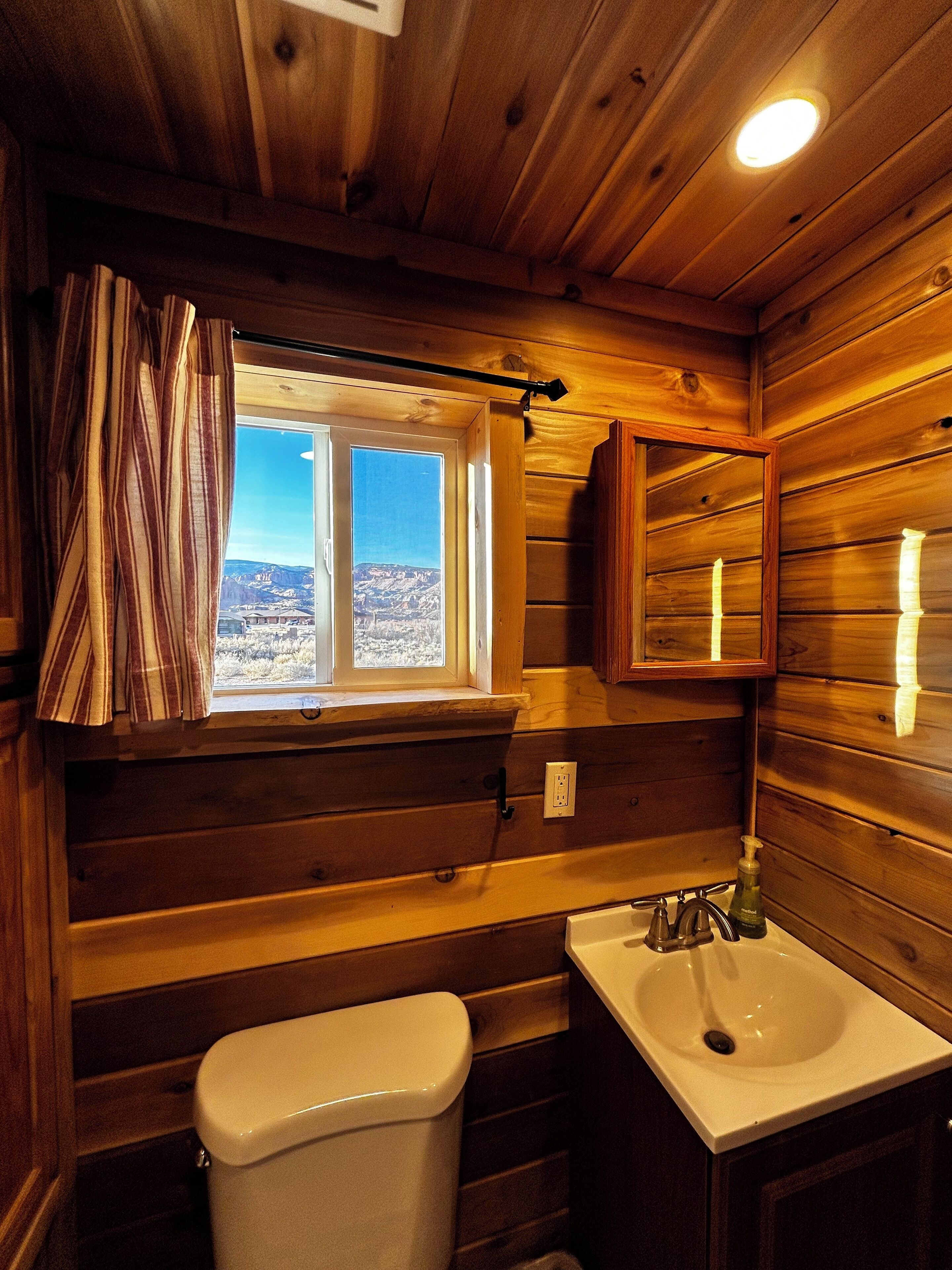 Une salle de bain rustique, avec des murs en bois, une fenêtre, un lavabo et des toilettes.