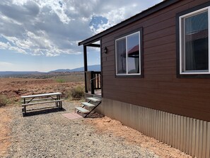 A wooden building with a porch, a picnic table, and a view of a desert landscape.