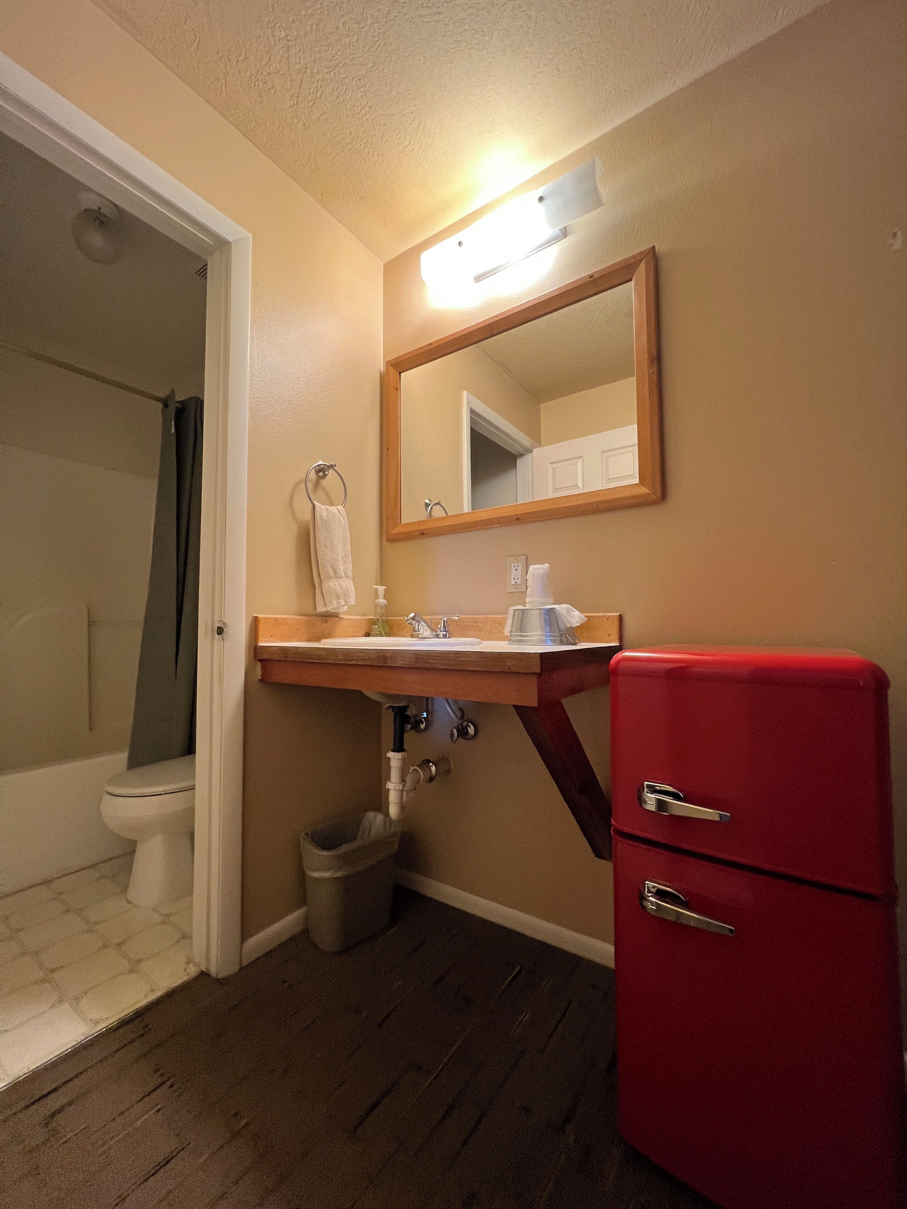 A bathroom with a toilet, sink, mirror, and a red cabinet.