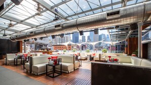 A modern lounge area with seating and tables, large windows offering city views, and a high ceiling with exposed ductwork. - The Godfrey Hotel Chicago (Chicago)