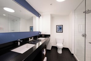 A modern bathroom with a black countertop, white sink, and a glass shower enclosure. - The Godfrey Hotel Chicago (Chicago)