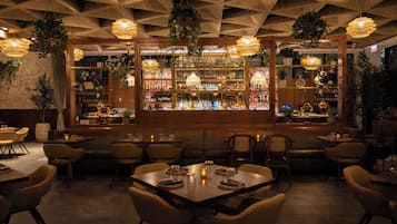 Un restaurante con zona de bar, con un diseño geométrico en el techo, plantas colgantes e iluminación cálida.