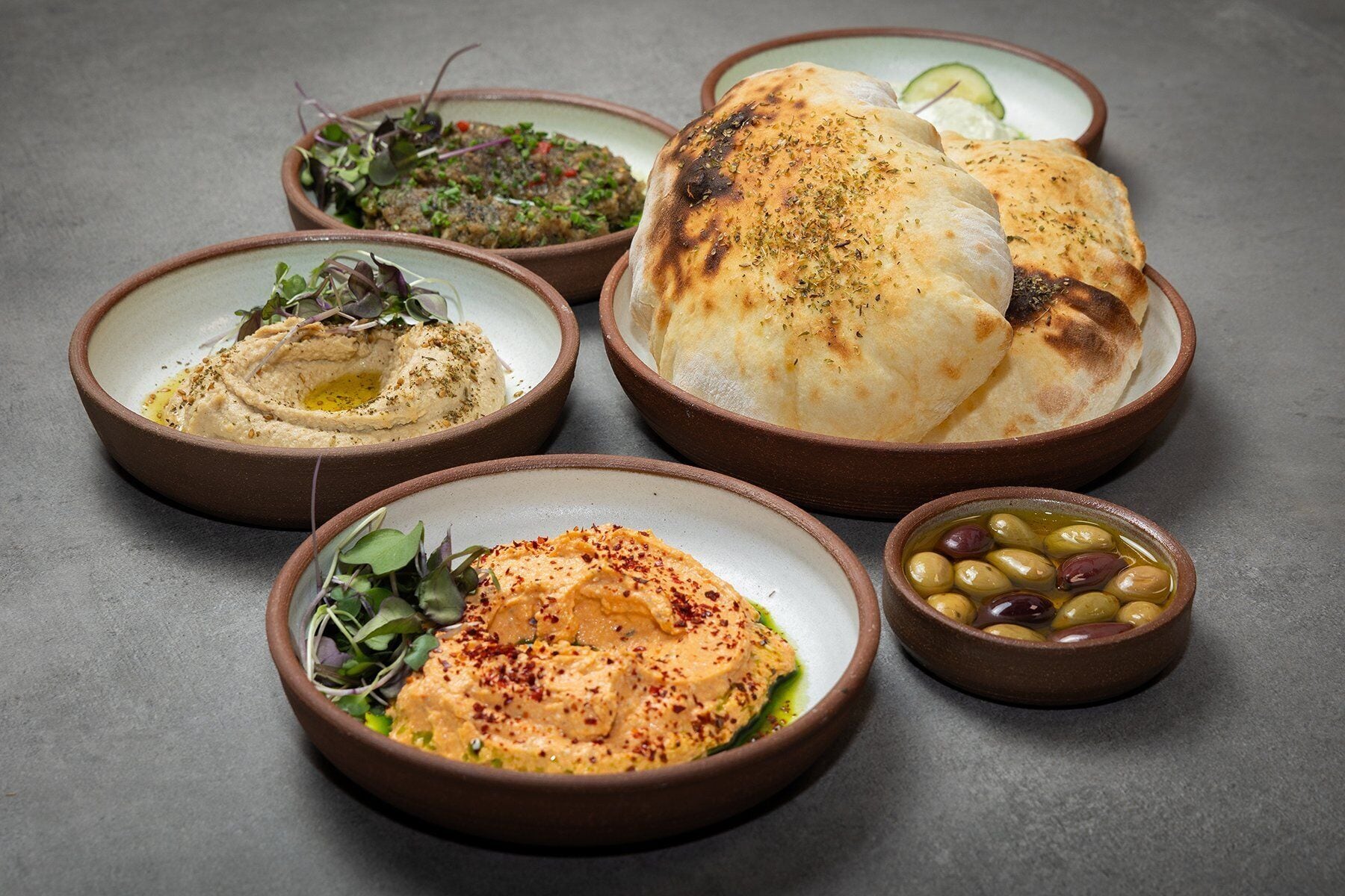 A table with various dishes including hummus, grilled meat, flatbread, and olives.
