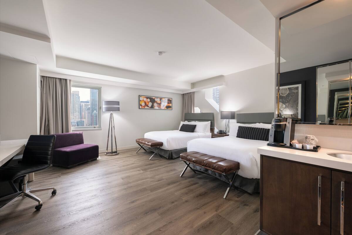 A modern hotel room with two beds, a desk, a chair, a sofa, and a large mirror.