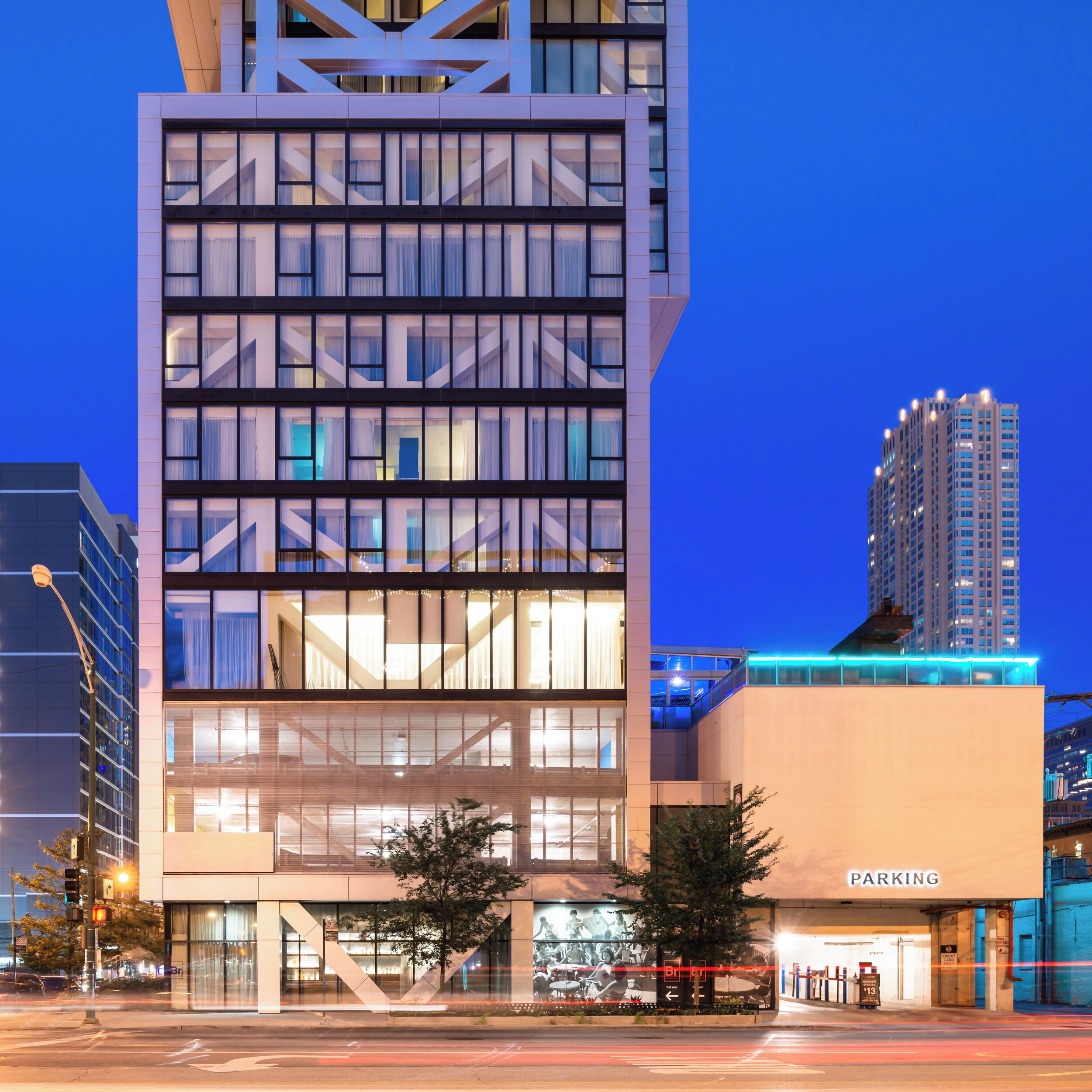 Un edificio moderno con fachada de vidrio, zona de estacionamiento visible y cielo despejado.