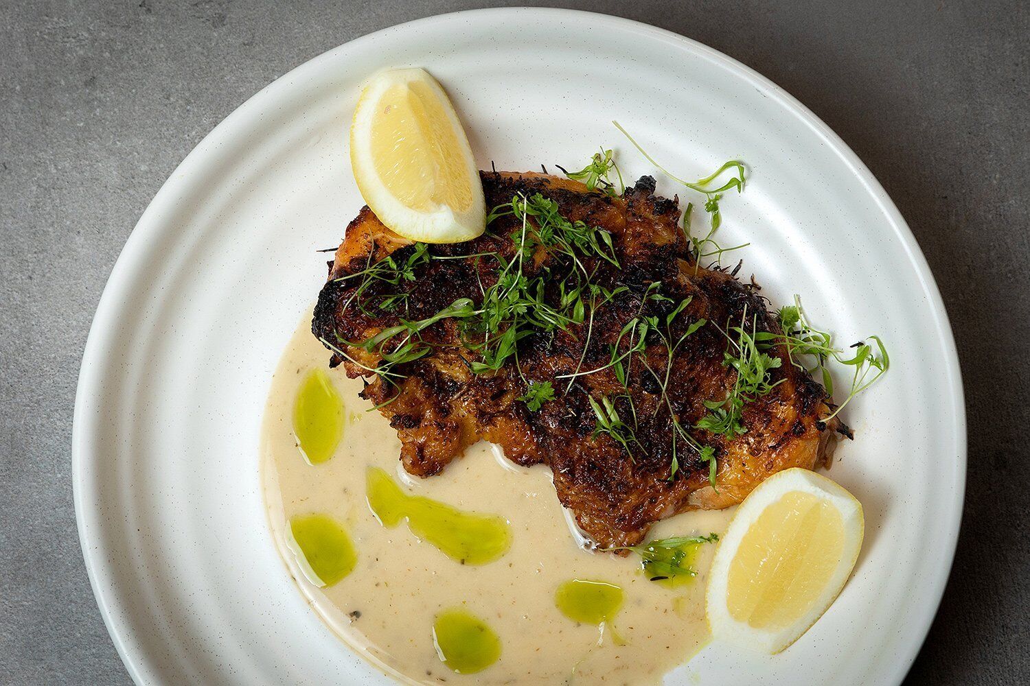 A plate with a grilled fish, lemon slices, and a creamy sauce.