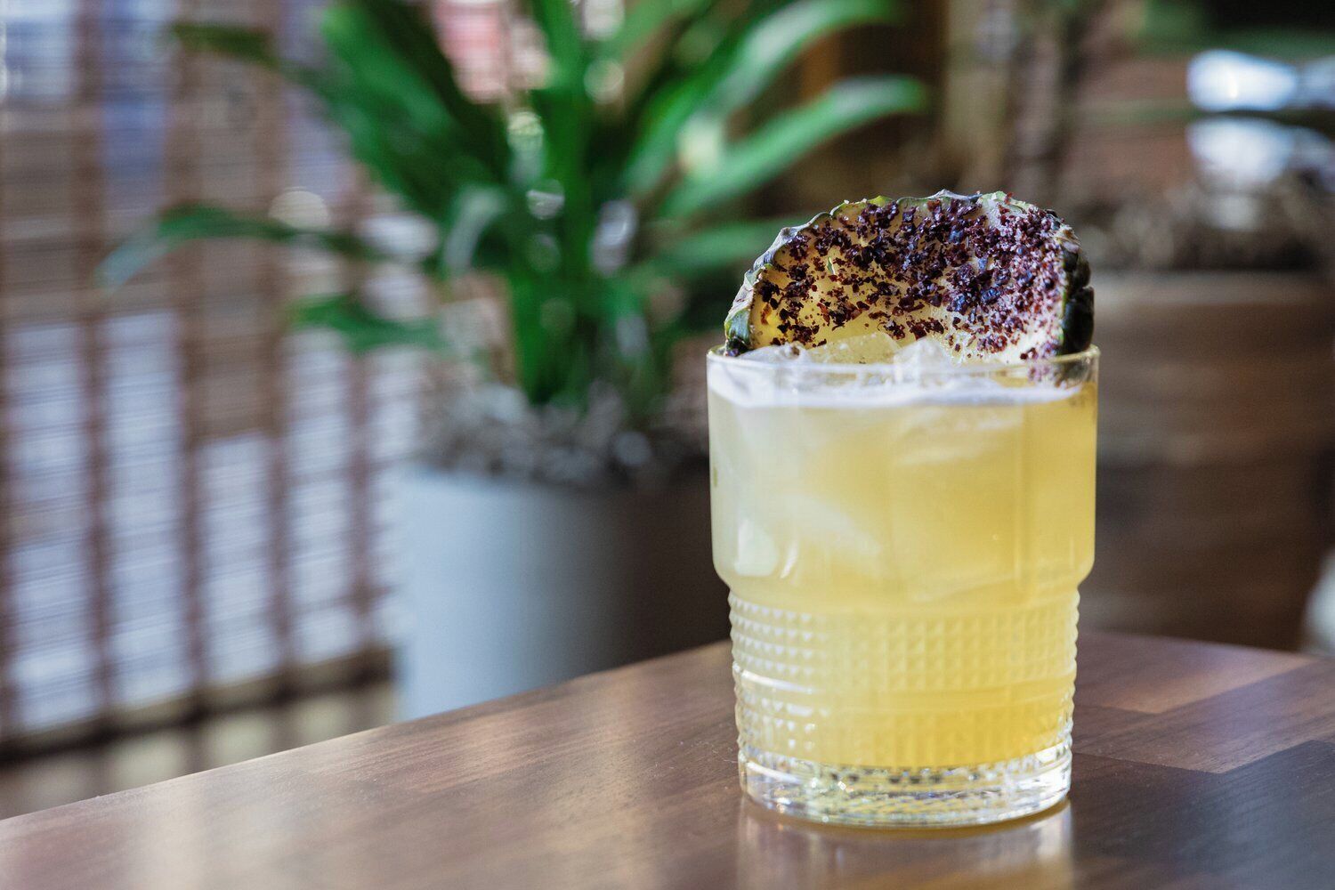 A glass of yellow beverage with a garnish on a wooden table.