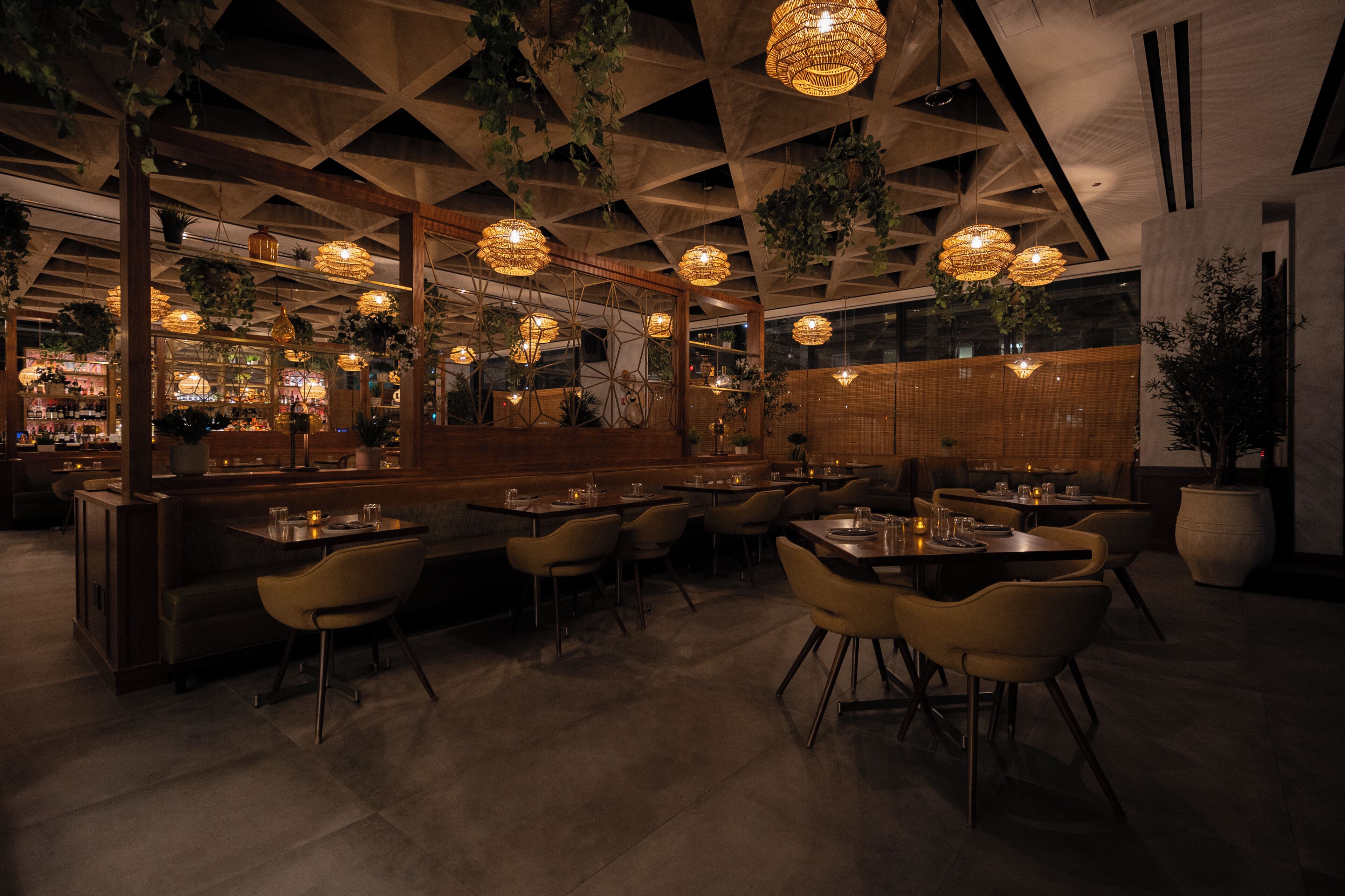 A restaurant with a modern interior, featuring hanging plants, wooden beams, and ambient lighting.