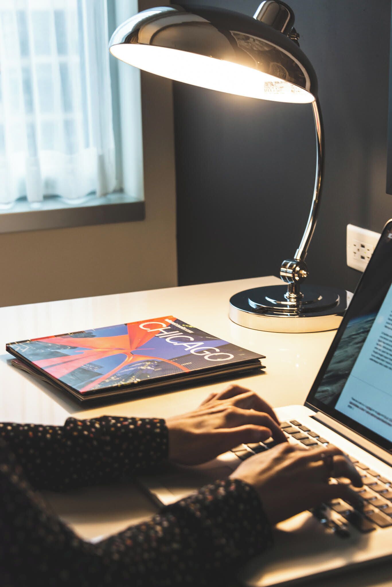 A desk with a laptop, a book, and a desk lamp.