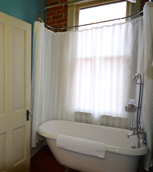 A bathroom with a freestanding bathtub, a window with sheer curtains, and a shower head.