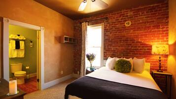 A bedroom with a brick wall, a ceiling fan, a bed with white bedding, a nightstand with a lamp, and a window with curtains.