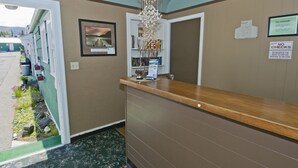 A reception area with a wooden counter, a hanging decorative light fixture, a framed picture on the wall, and a small garden outside. - All View Motel (Port Angeles)