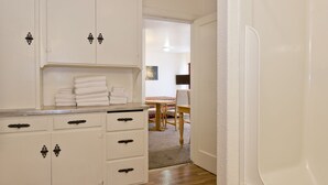 A clean, white kitchen with wooden cabinets and a countertop. There is a stack of folded towels on the counter. - All View Motel (Port Angeles)