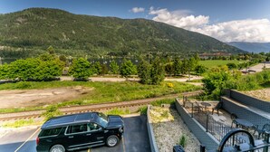 A black SUV parked on a road with a scenic view of a lake, mountains, and a small town in the background. - Prestige Inn Nelson (Nelson)