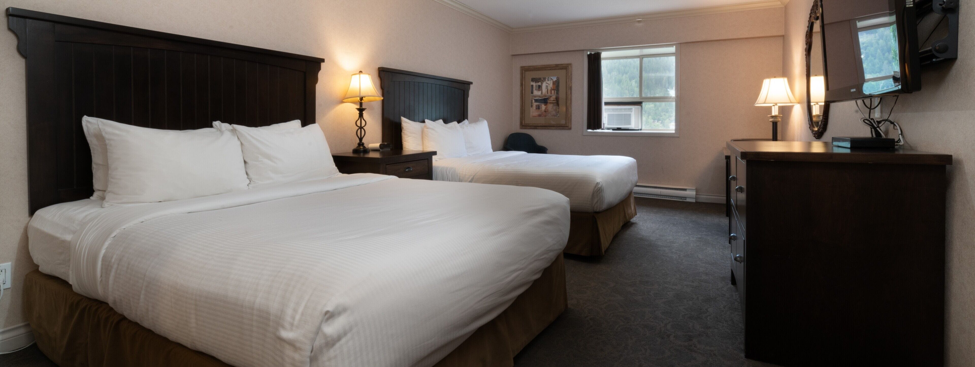 Une chambre d’hôtel avec deux lits, un bureau, une commode et une fenêtre donnant sur un beau paysage.