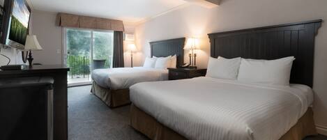 A hotel room with two beds, a TV, a desk, and a balcony with a view.