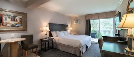Une chambre d’hôtel avec un lit, deux tables de chevet avec des lampes, une chaise, une petite table ronde et un tableau au mur.