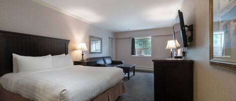 A hotel room with a large bed, a desk, a chair, a flat-screen TV mounted on the wall, and a window with curtains.