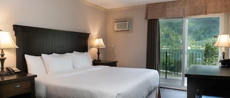 A hotel room with a large bed, two bedside tables with lamps, a desk, and a view of a balcony with a railing.