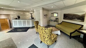 A reception area with a reception desk, a sofa, two patterned chairs, a coffee table, and a painting on the wall. - Prestige Inn Nelson (Nelson)