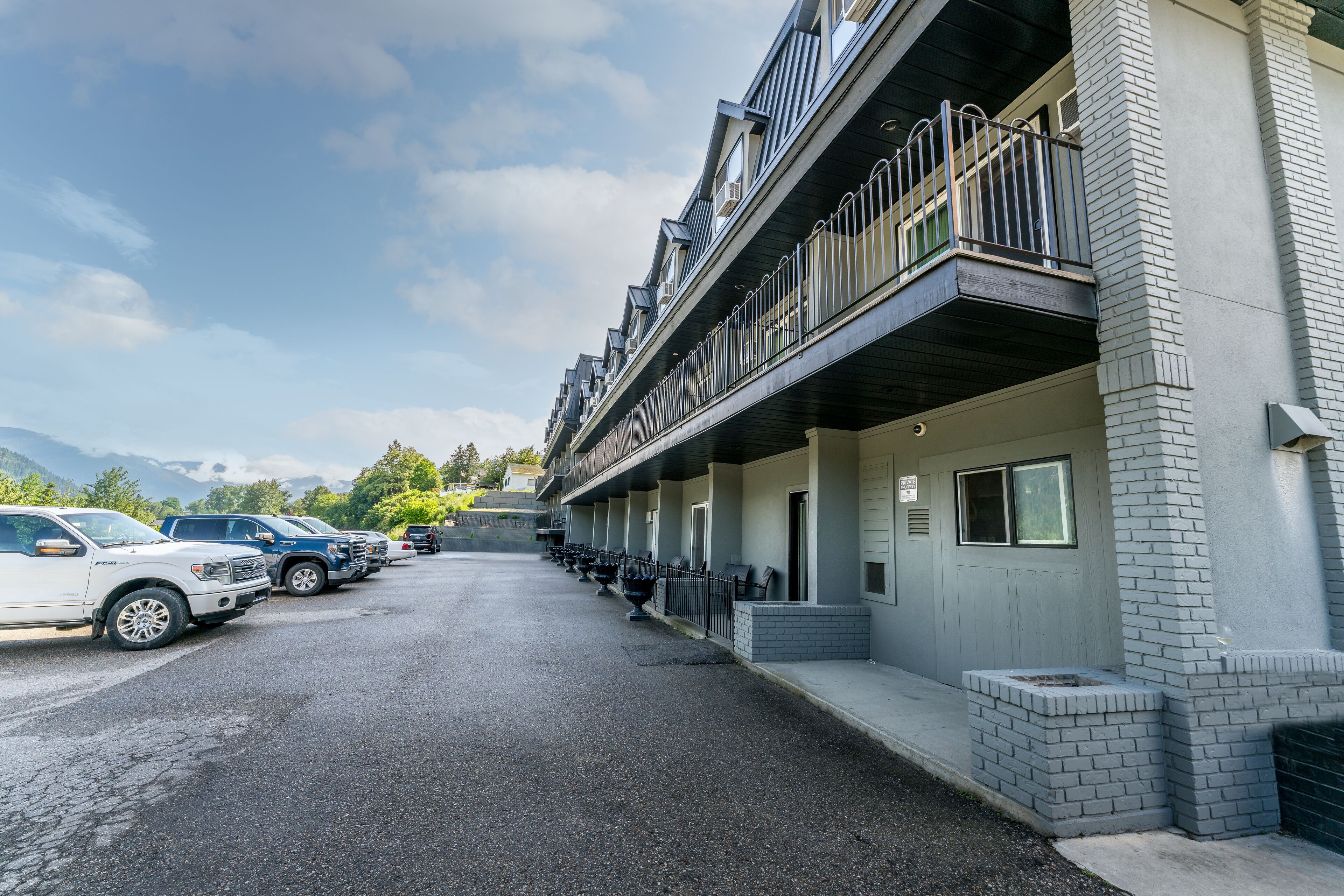 A multi-story building with a row of balconies and a parking lot with several cars.