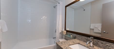 A modern bathroom with a bathtub, toilet, and granite countertop sink.