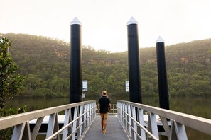 A person walking on a bridge with two large cylindrical structures on either side, overlooking a forested area. - Wisemans Retreat (Wisemans Ferry)