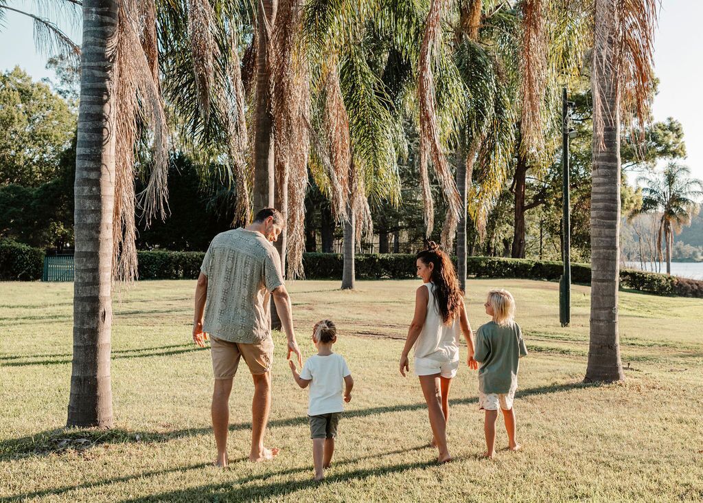 A family walking on a grassy area with palm trees and a body of water in the background.