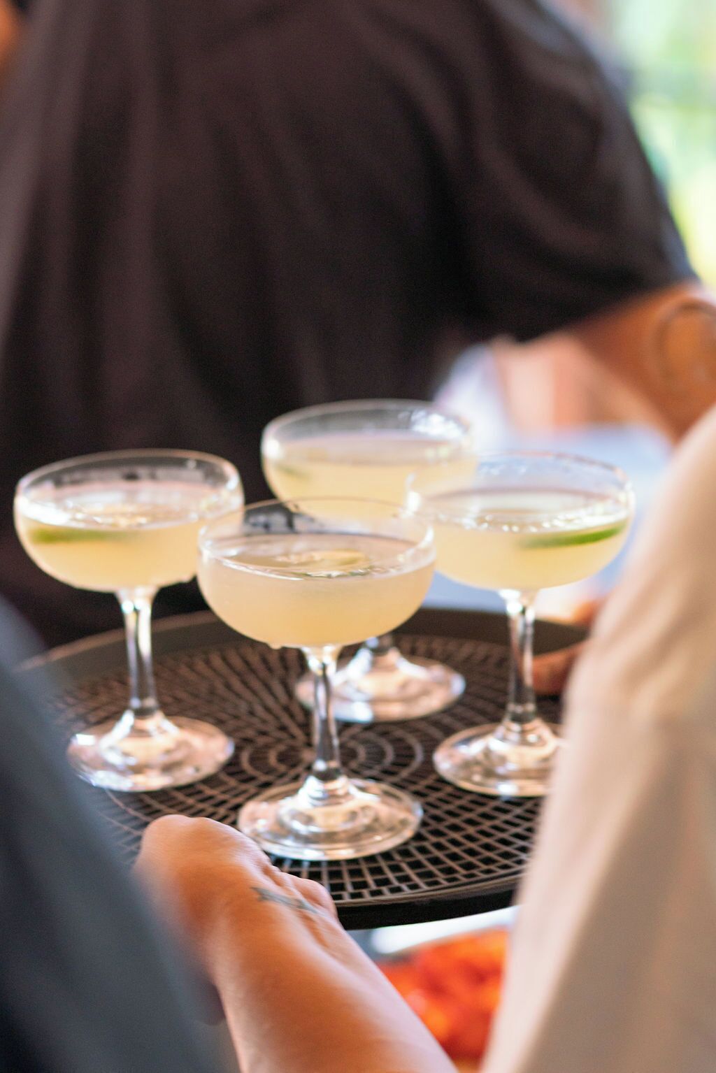 A tray with four glasses of a light-colored beverage, possibly a cocktail, with lime wedges.