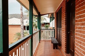A covered balcony with a bench, brick walls, and a view of neighboring buildings and palm trees. - Wisemans Retreat (Wisemans Ferry)
