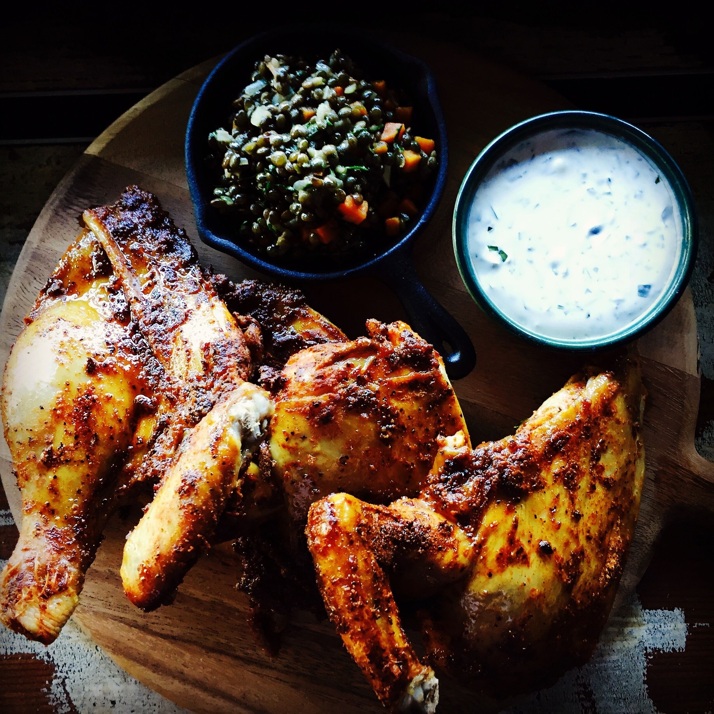 Une planche en bois sur laquelle sont disposées des ailes de poulet grillées, un bol de légumes variés et un bol de sauce blanche.