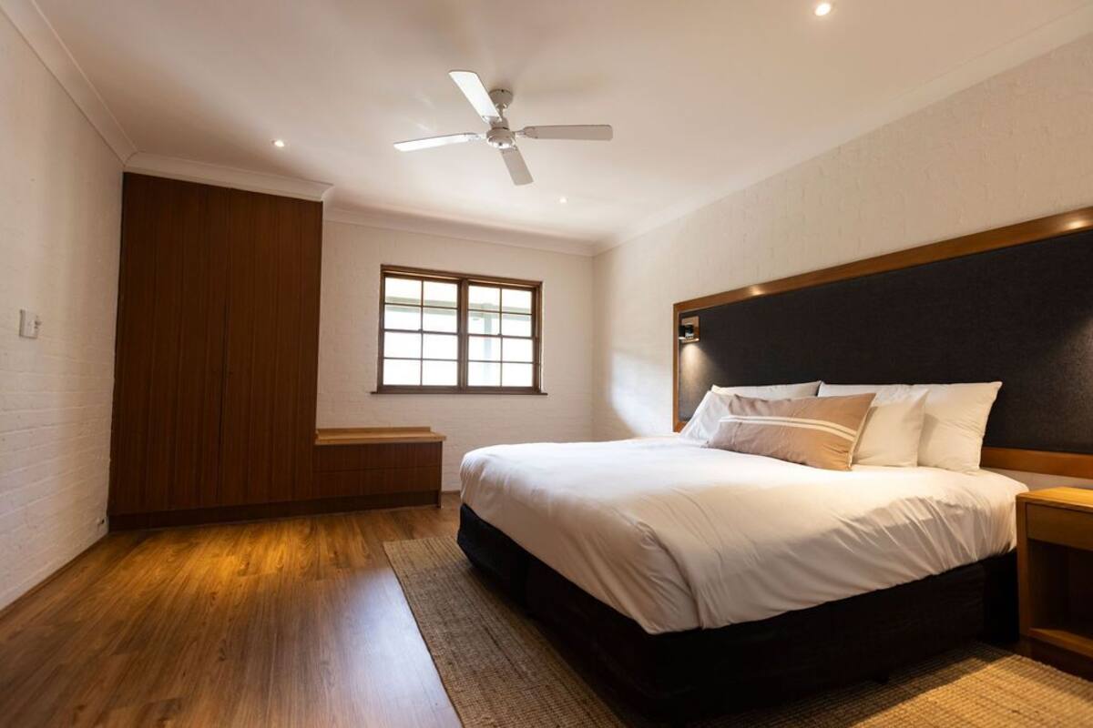 A bedroom with a bed, a ceiling fan, a window, and wooden flooring.